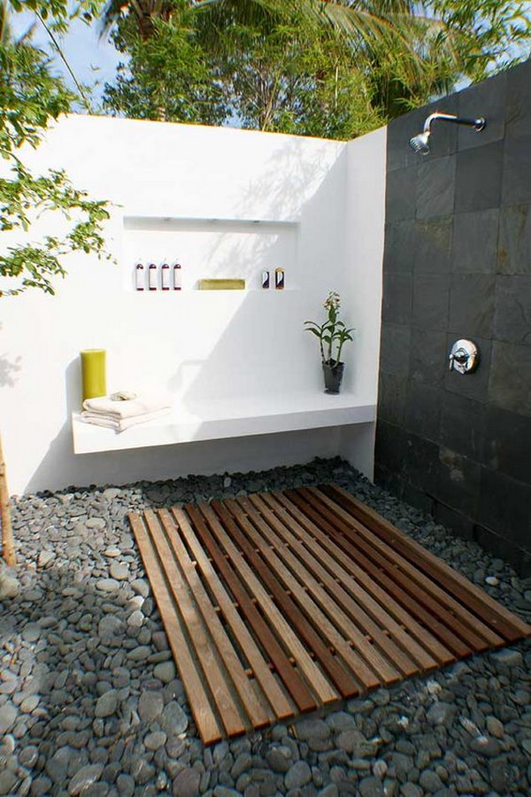 Covered outdoor shower area with cobblestones and wall bench. 