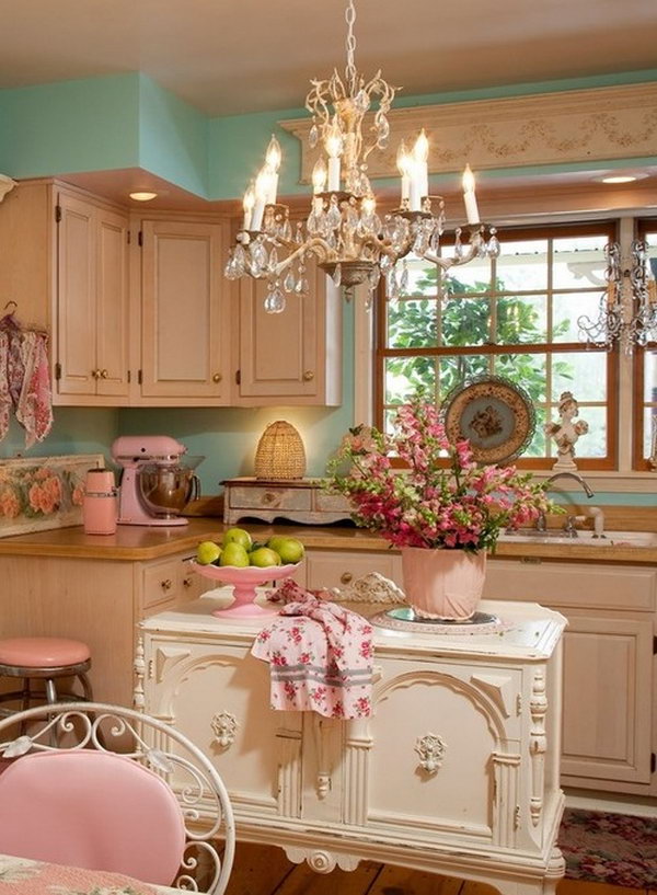 Shabby chic look. This beautiful white French island in vintage style gives this cream and pastel colored kitchen elegant and chic feelings. It really fits everything, the beautiful ornate elements, which are painted over in a soft cream, a chandelier hangs from the ceiling and retro kitchen utensils in pink enamel and so on. 