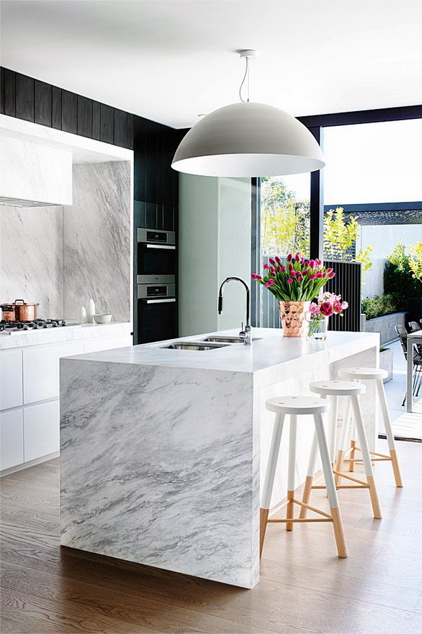     Stylish black and white kitchen. In this kitchen, the black and white contrast has been retained throughout the decor, including the marble waterfall countertop. The lamp and the custom-made stools give this kitchen an outstanding feeling of style and glamor.