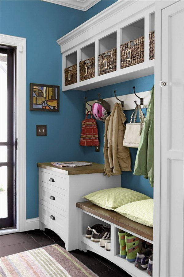     White and blue mud room. This small mud room is beautifully equipped with a white and blue color palette, basket storage, large hooks for hanging coats, easy to clean black floor and bench. 