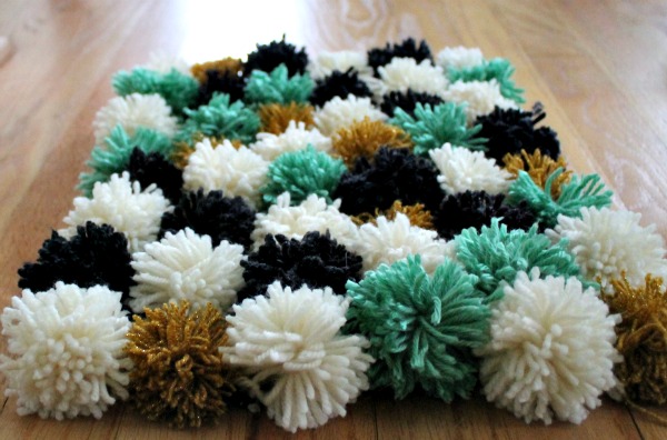 DIY pom pom carpet. Choose a thread color and wrap it around, tie a thread around the middle and cut off the ends to make the pompom. Create the carpet with pompoms according to your wishes. Arrange pieces of yarn in a grid and tie each pompom together to create your design and add color, texture and comfort to your dormitory.