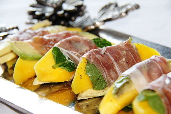 Mango bites wrapped in ham. Serve your guests with this quickly served starter. Cut the mango into slices, place each slice on rocket and basil. Wrap slices of mango in a strip of ham. Add some pepper for ingredients.