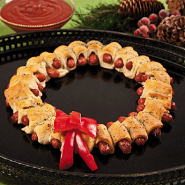 Mini sausage wreaths. Cut the prepared pizza into 32 pieces and wrap a strip of dough around the mini sausage. Bake until the color turns gold. Add butter with rosemary over the sausages. Place in a wreath shape and add the red pepper bow to the decoration to celebrate your Christmas party. 
