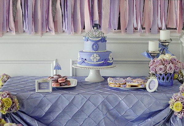 Sofia inspired princess party. The backdrop of the dessert table, the glittering crown banners of the princess, the toppers of the princess dresses and many other favors complement the romantic lavender taste.