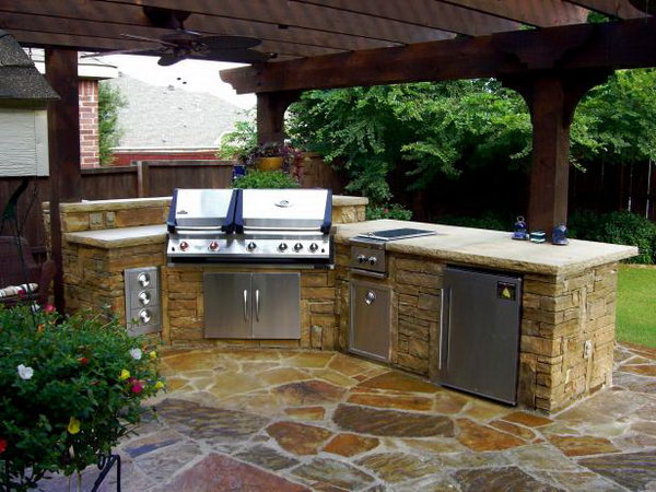 This stone outdoor kitchen has a fridge, grill, sink and storage space. It looks simple, but fully functional. The wooden roof and the stone structure are ideal and cool when cooking and eating in the summer night. 