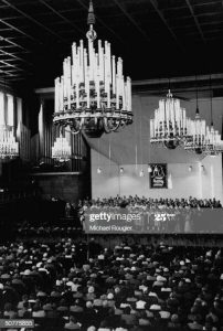 Huge chandeliers light the room, while people enjoy the show. News .