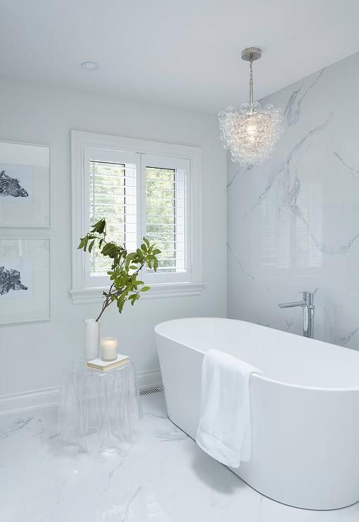 A glass bubbles chandelier hangs over a modern oval bathtub paired .
