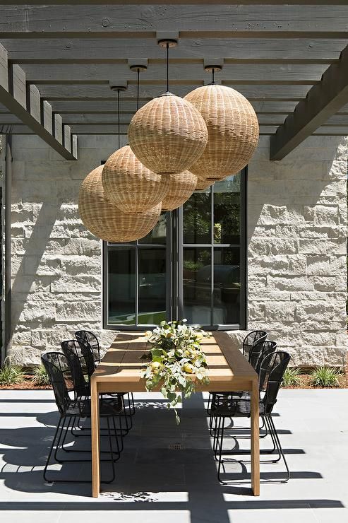 Wicker lanterns hang from a gray wood pergola over a blond teak .